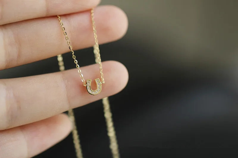 Colar dourado ferradura delicado segurado entre os dedos, prata 925 banhada a ouro – Loja Simplicité