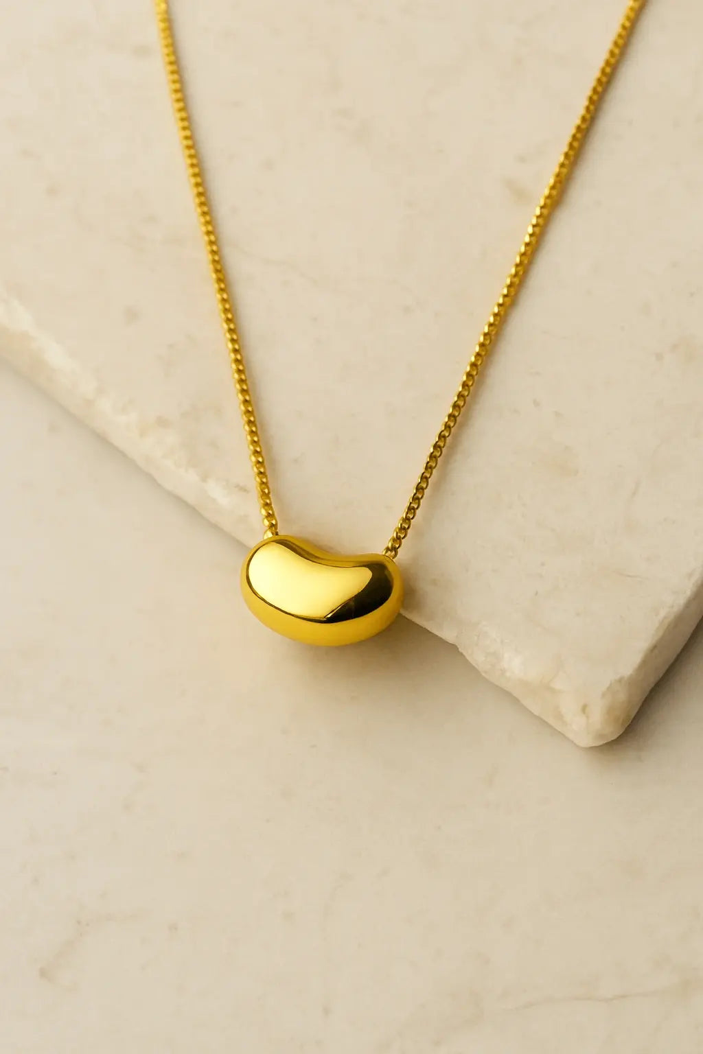 Colar minimalista pingente semente dourada orgânico sobre pedra natural clara