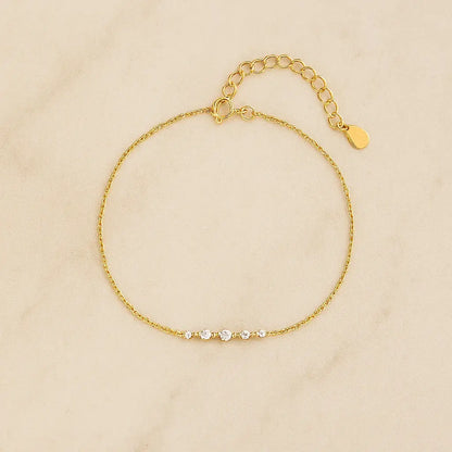 Pulseira minimalista barra dourada cravejada sobre pedra natural clara