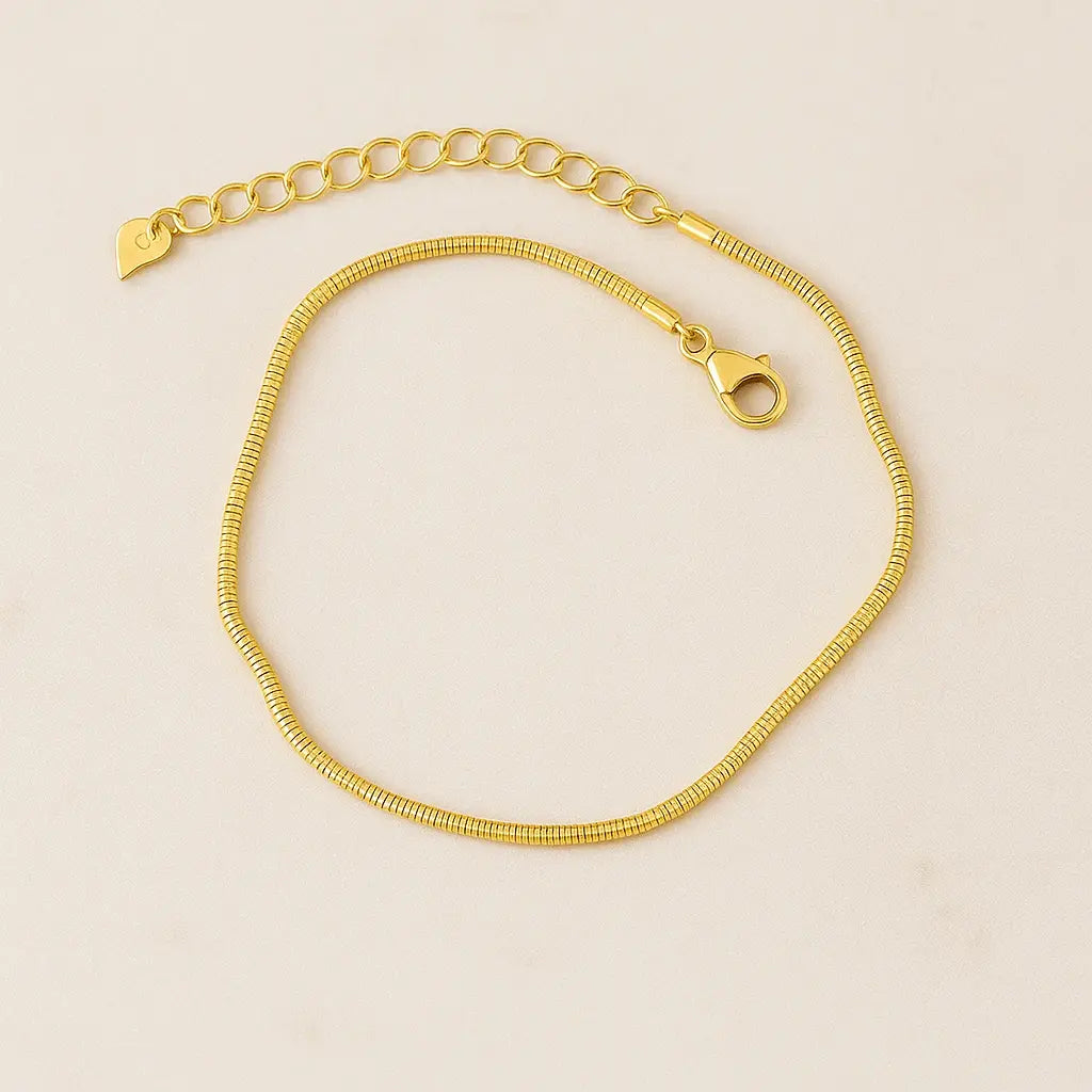 Tornozeleira minimalista snake dourada sobre pedra natural clara