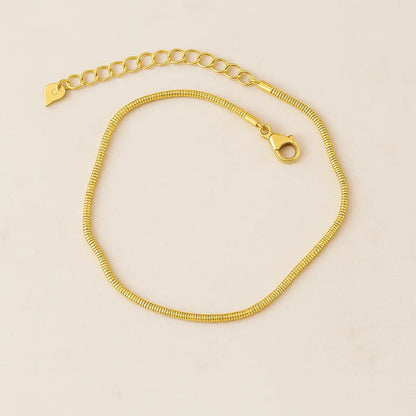 Tornozeleira minimalista snake dourada sobre pedra natural clara